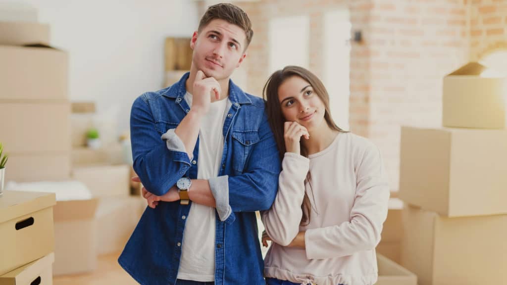 Couple standing in front of a recently moved-in house wondering if they should start a family