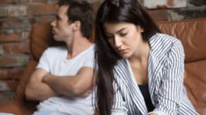 A woman looks down, concerned. Her boyfriend looks away angrily