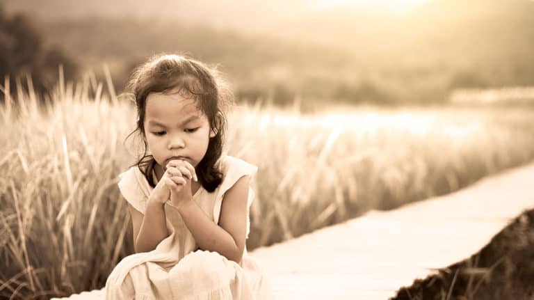 Sad child sitting alone on wall outdoors