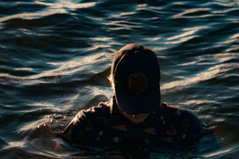 Fully clothed man in baseball had stands nearly immersed in water depicting depression