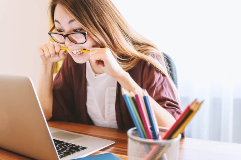 Young Asian woman sitting at her computer, biting her pencil in excitement or frustration