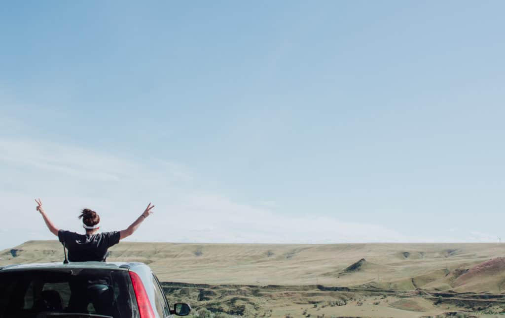 Are All Religions Equal - Girl standing in car through sun roof and viewing a vast plain