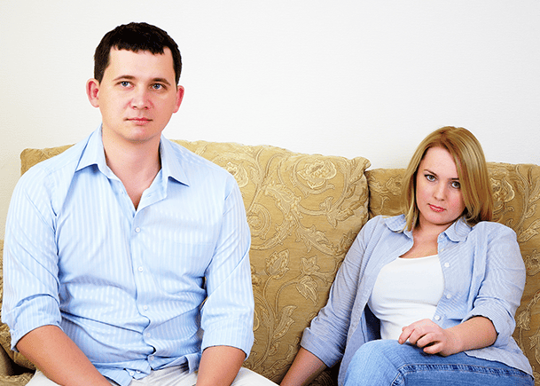 Young-married-couple-sitting-on-couch-not-looking-at-each-other-and-cannot-agree