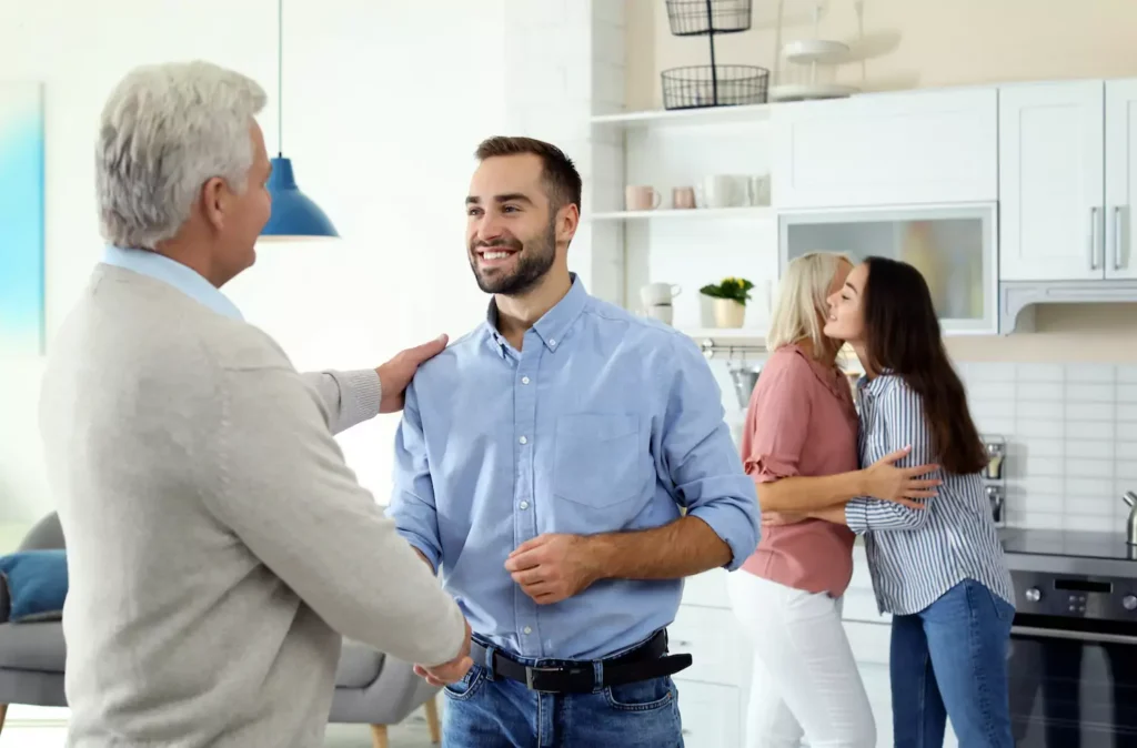 A father in law greets his son in law as the daughter embraces her mother in the background. Check out these 12 questions every father in law should ask his future son in law.