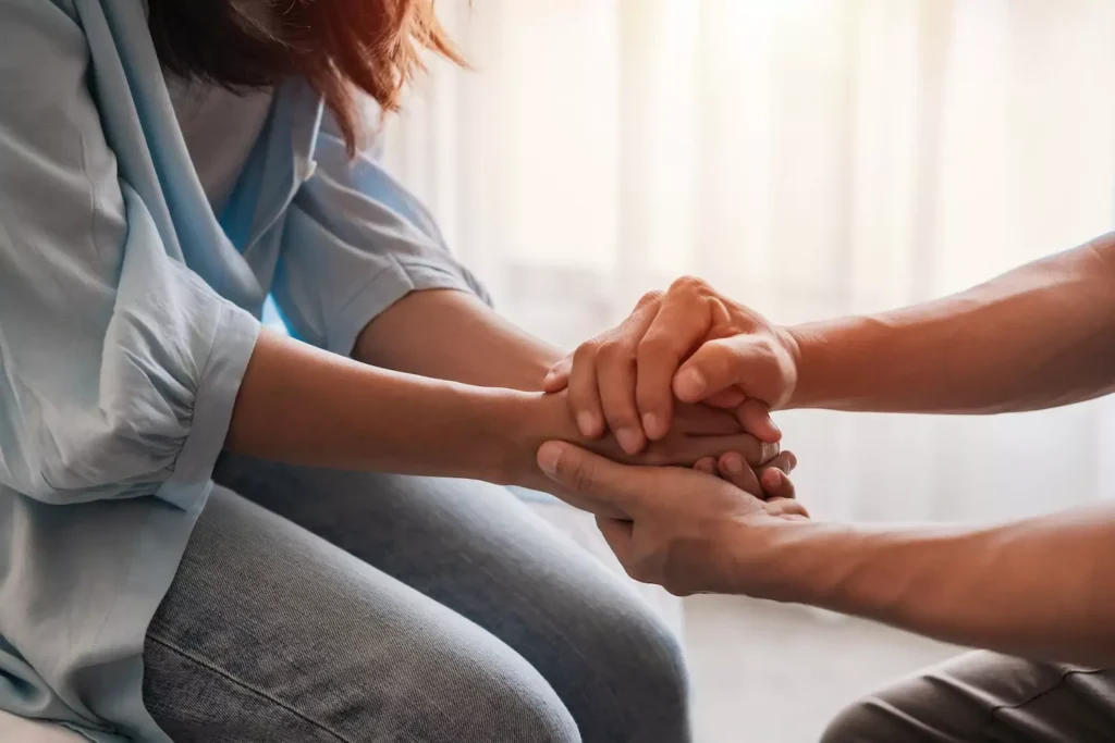 A couple sitting across from each other hold hands, in support of each other. Be on the lookout for warning signs of mental health issues.